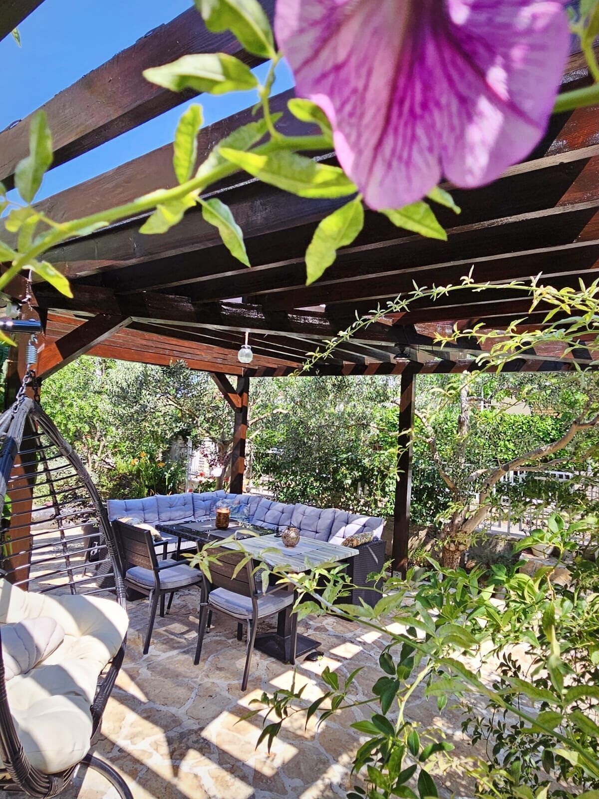 An outdoor patio with a wooden pergola, a cushioned seating area, and a hanging light fixture.