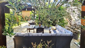 An outdoor seating area with wicker furniture and a hanging chair, surrounded by olive trees and potted plants. - Apartments Marijana (Vodice)