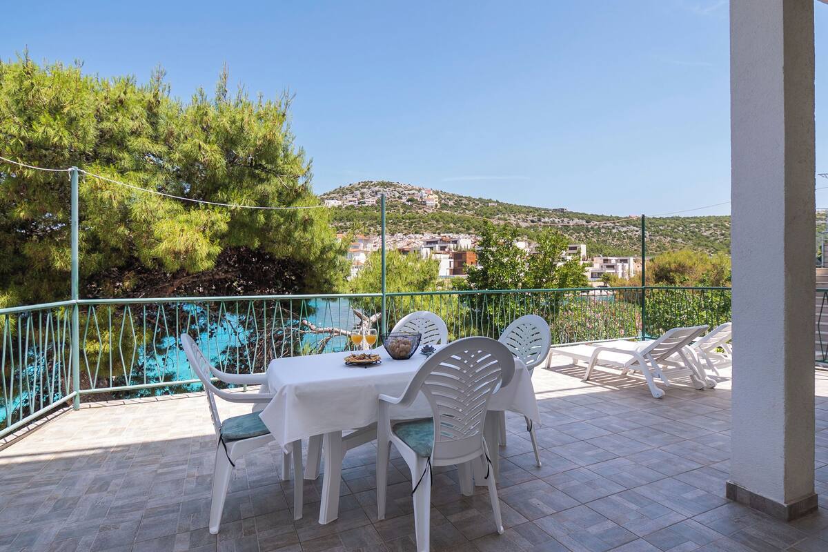 A terrace with a table and chairs, overlooking a swimming pool and a hillside town.