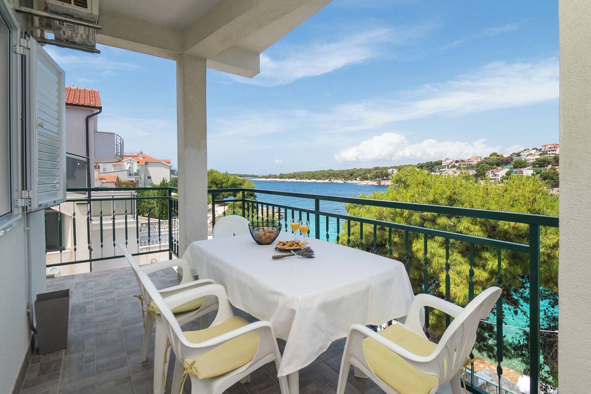 A balcony with a table set for two, overlooking a coastal view.