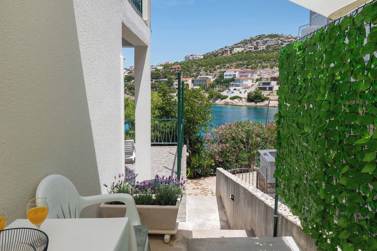 A balcony with a view of a coastal town, a table with drinks, and a potted plant.