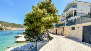 A coastal building with a stone-paved walkway, a tree, and a clear view of the sea. - Apartments Ivica (Bilo)