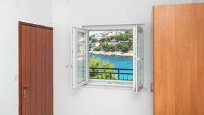A room with a wooden door, a window with a view of a coastal area, and a balcony railing. - Apartments Ivica (Bilo)