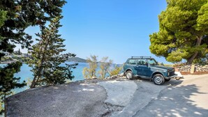 A blue SUV parked on a paved area with a view of a body of water and trees. - Apartments Kresimir (Razanj)