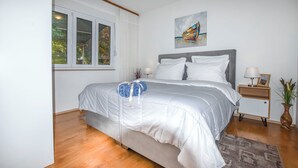 A bedroom with a bed, a nightstand, a lamp, a painting, and a window with curtains. - Apartments Kresimir (Razanj)