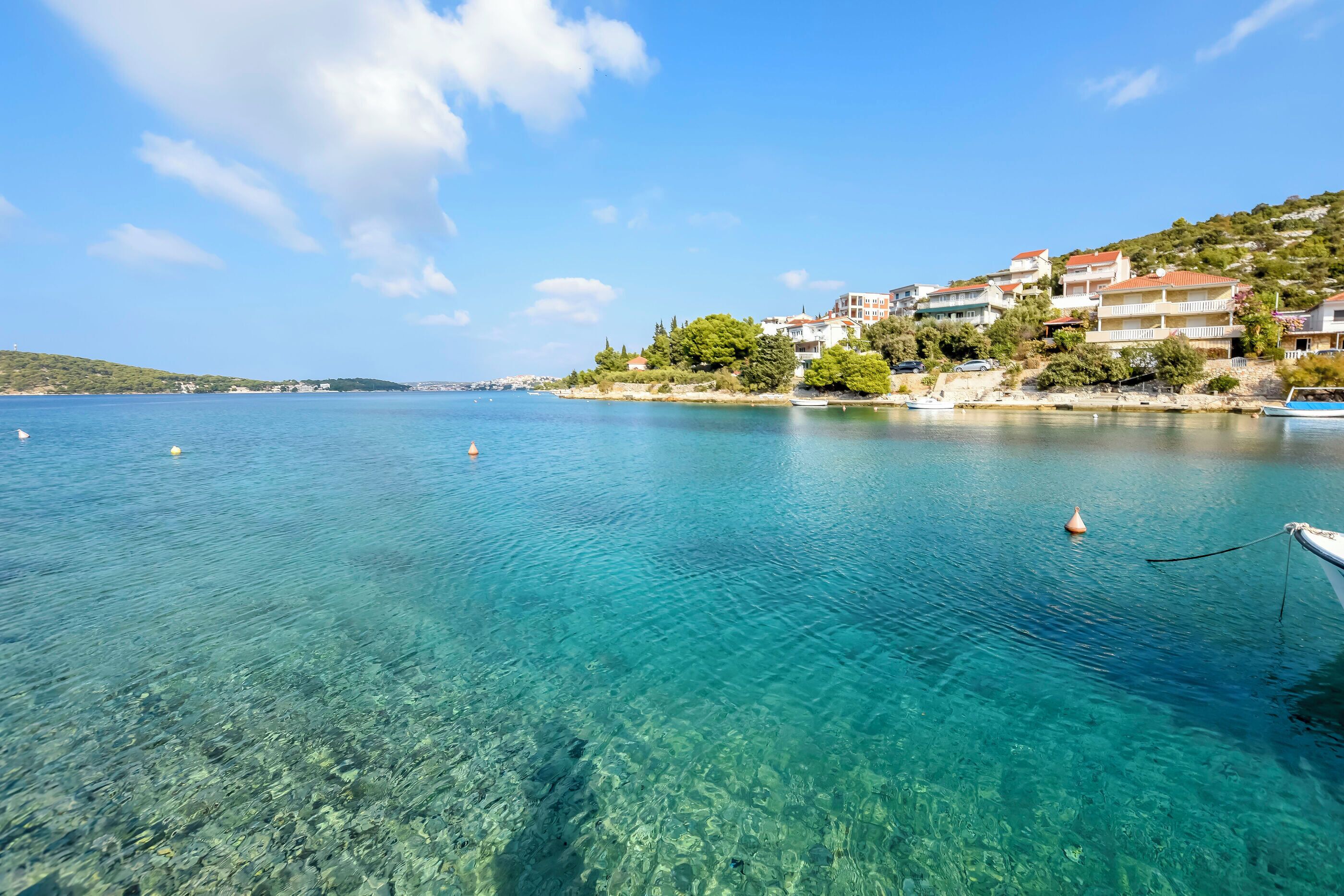 Uma vila costeira com águas turquesa cristalinas, edifícios numa encosta e um barco ancorado perto da costa.
