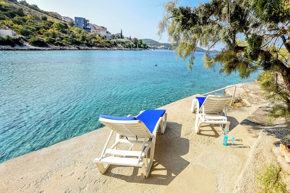 A seaside view with two sun loungers on a sandy beach, overlooking a calm sea.