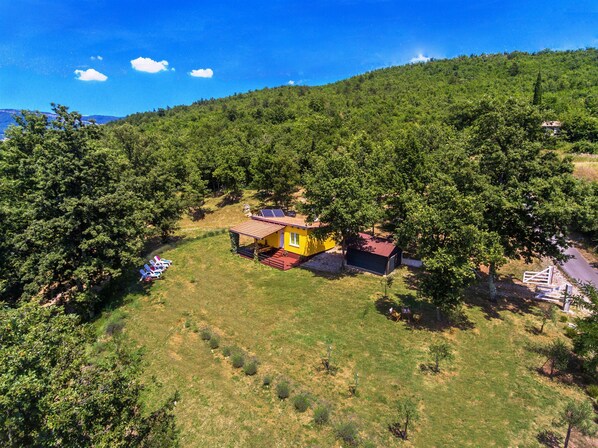 Une petite maison jaune, avec un toit rouge, entourée d’arbres sur le flanc d’une colline.