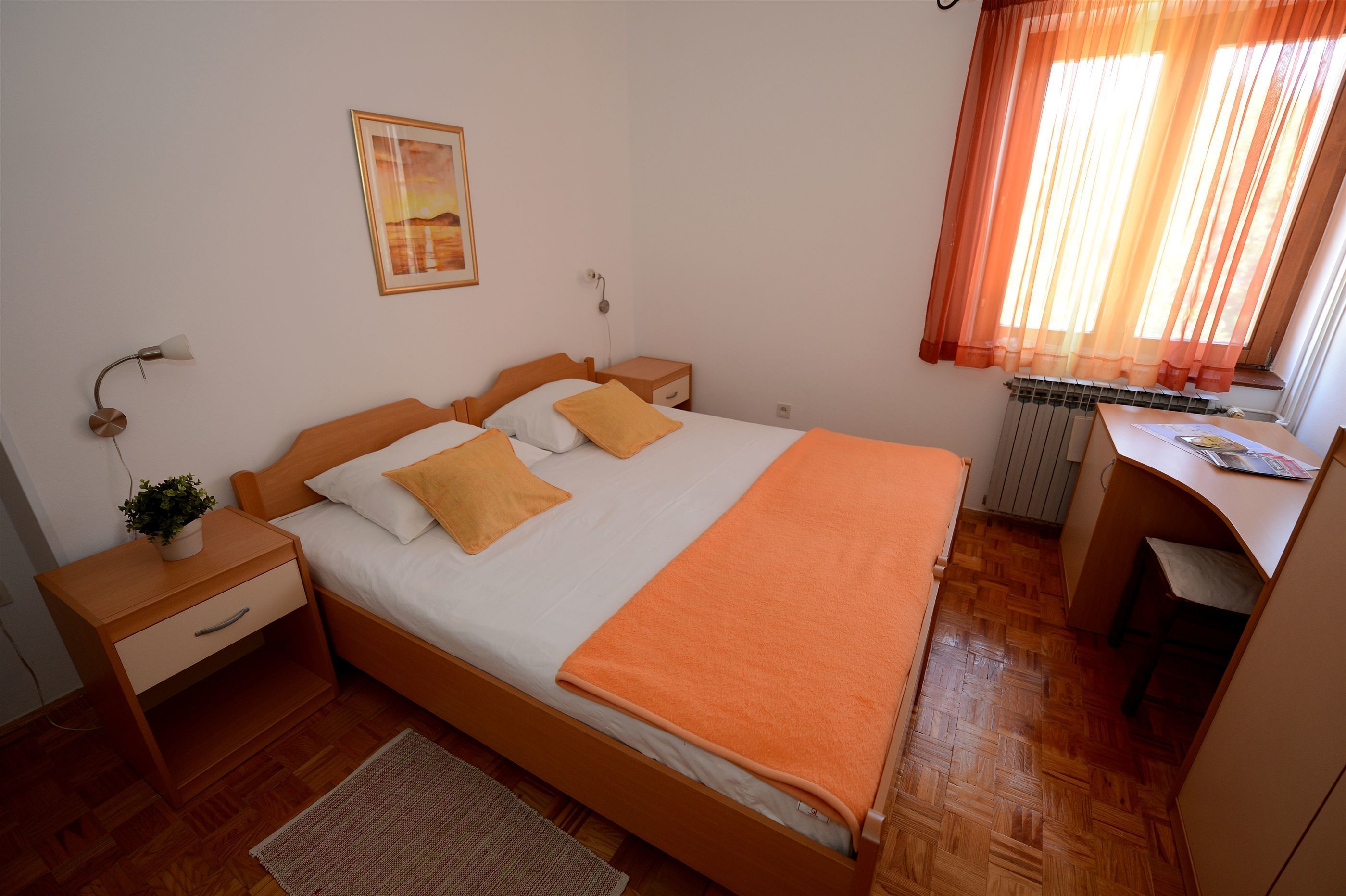 A neatly arranged bedroom with a bed, bedside tables, a desk, and a radiator.