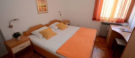 A neatly arranged bedroom with a bed, bedside tables, a desk, and a radiator.