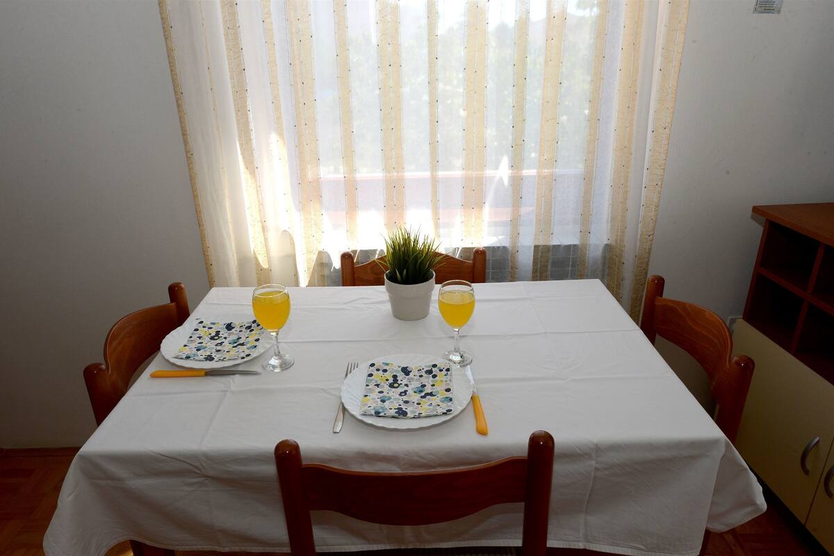 A dining table set with plates, cutlery, and glasses, with a potted plant in the center.