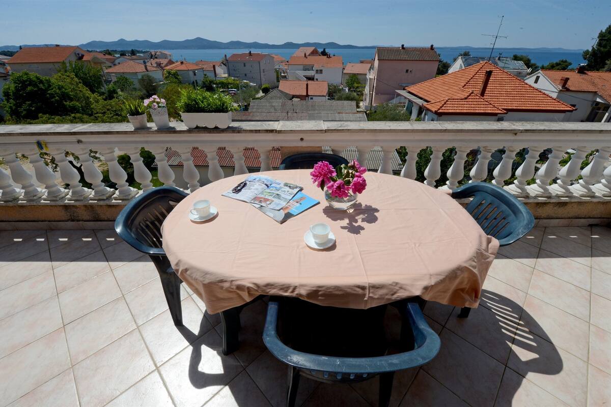 A round table with a beige tablecloth, two chairs, a vase with pink flowers, and a menu on the table.