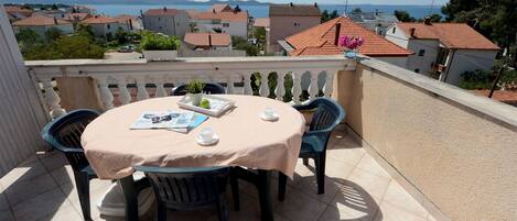 A terrace with a table set for two, overlooking a coastal town with houses and mountains in the distance.