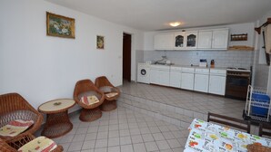 Une cuisine avec des meubles blancs, un lave-linge et un coin repas comprenant des chaises et une table en osier.