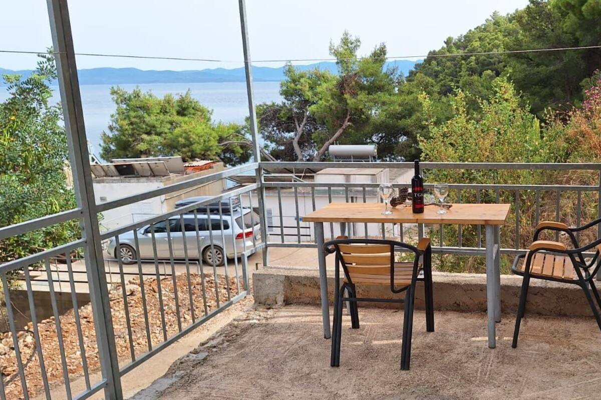 A balcony with a table and chairs, overlooking a road with parked cars and a view of trees and mountains.