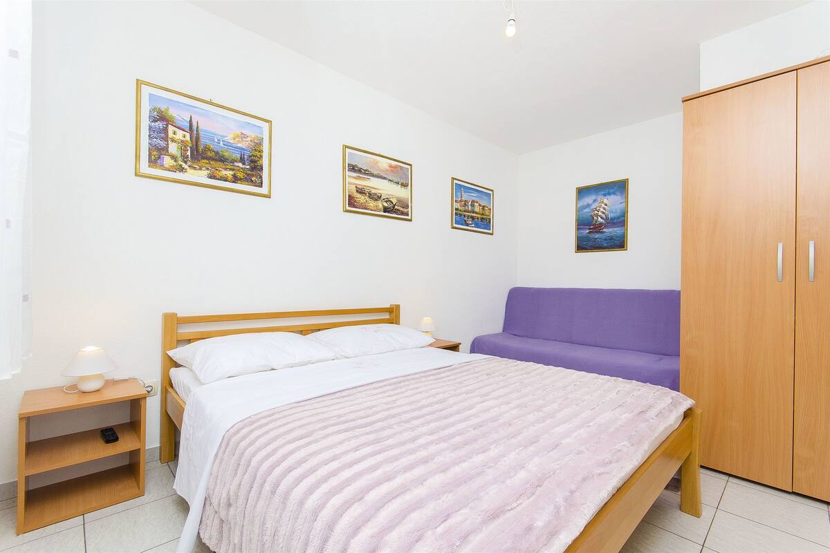 A bedroom with a bed, a nightstand, a purple sofa, and a wardrobe.