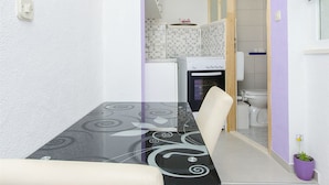 A compact kitchen with a dining table, chairs, and a small oven. - Apartment Antonio (Bogomolje)