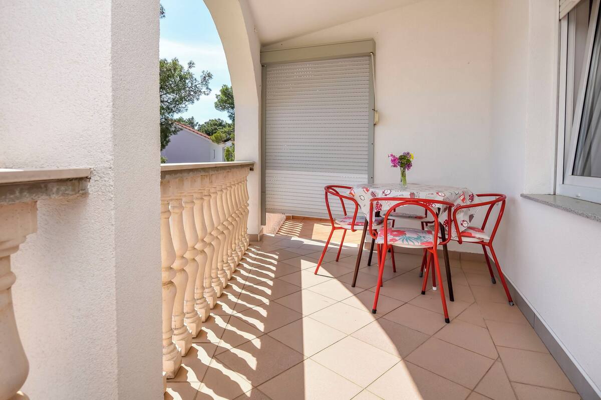 A balcony with a table and chairs, a closed shutter, and a view of the outside.