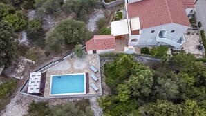 Eine Luftaufnahme eines Anwesens mit Schwimmbad, überdachter Terrasse und einem Haus mit rotem Ziegeldach.