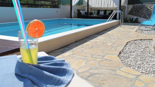 Ein Poolbereich mit klarem, blauem Pool, Liegestühlen und einem Getränk mit Strohhalm und Orangenscheibe.