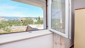 A room with a large window offering a view of a coastal landscape, a wooden floor, and a white wall. - Apartments Mirta (Razanj)