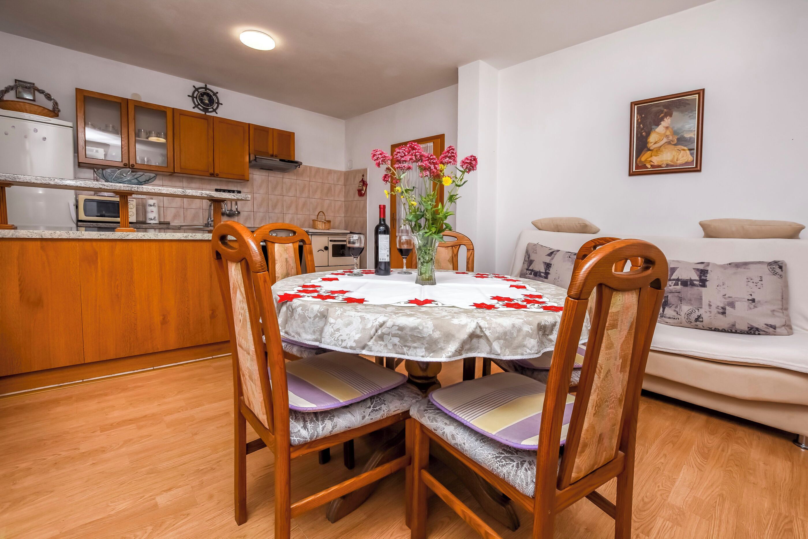 A dining area with a round table, wooden chairs, and a vase with flowers.