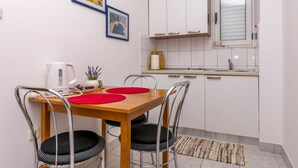 Eine kleine Küche mit weißen Schränken, einem Holztisch mit vier Stühlen und einem Fenster über der Spüle.
