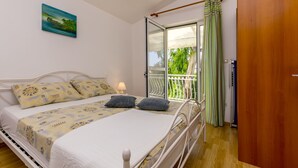 Ein Schlafzimmer mit einem Bett, einem Nachttisch, einem Fenster mit Blick auf Grünflächen und einer Tür.