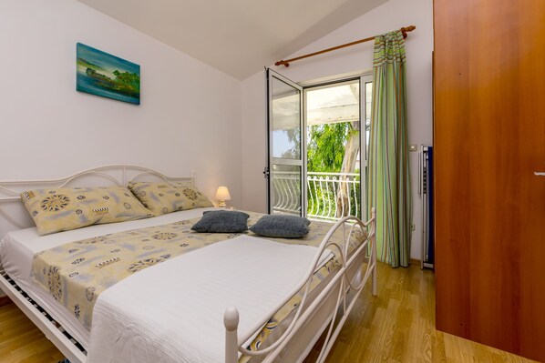 A bedroom with a bed, a nightstand, a window with a view of greenery, and a door.