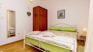 Ein Schlafzimmer mit Bett, Kleiderschrank, Nachttisch mit Lampe, Spiegel und einem gerahmten Bild an der Wand.