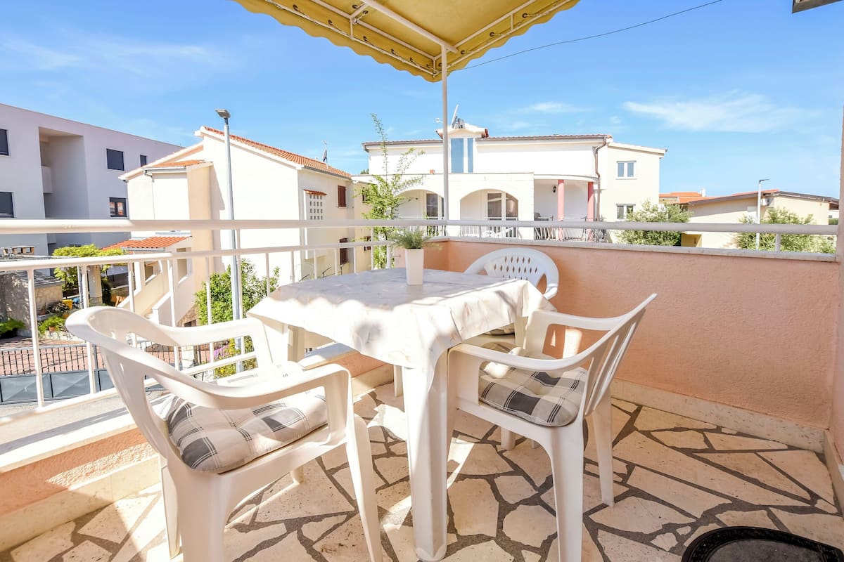 A balcony with a table and chairs, a yellow awning, and a view of neighboring buildings.