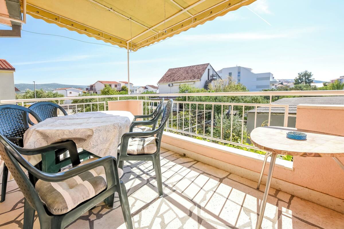 A balcony with a table and chairs, a small round table, and a view of buildings and greenery in the background.