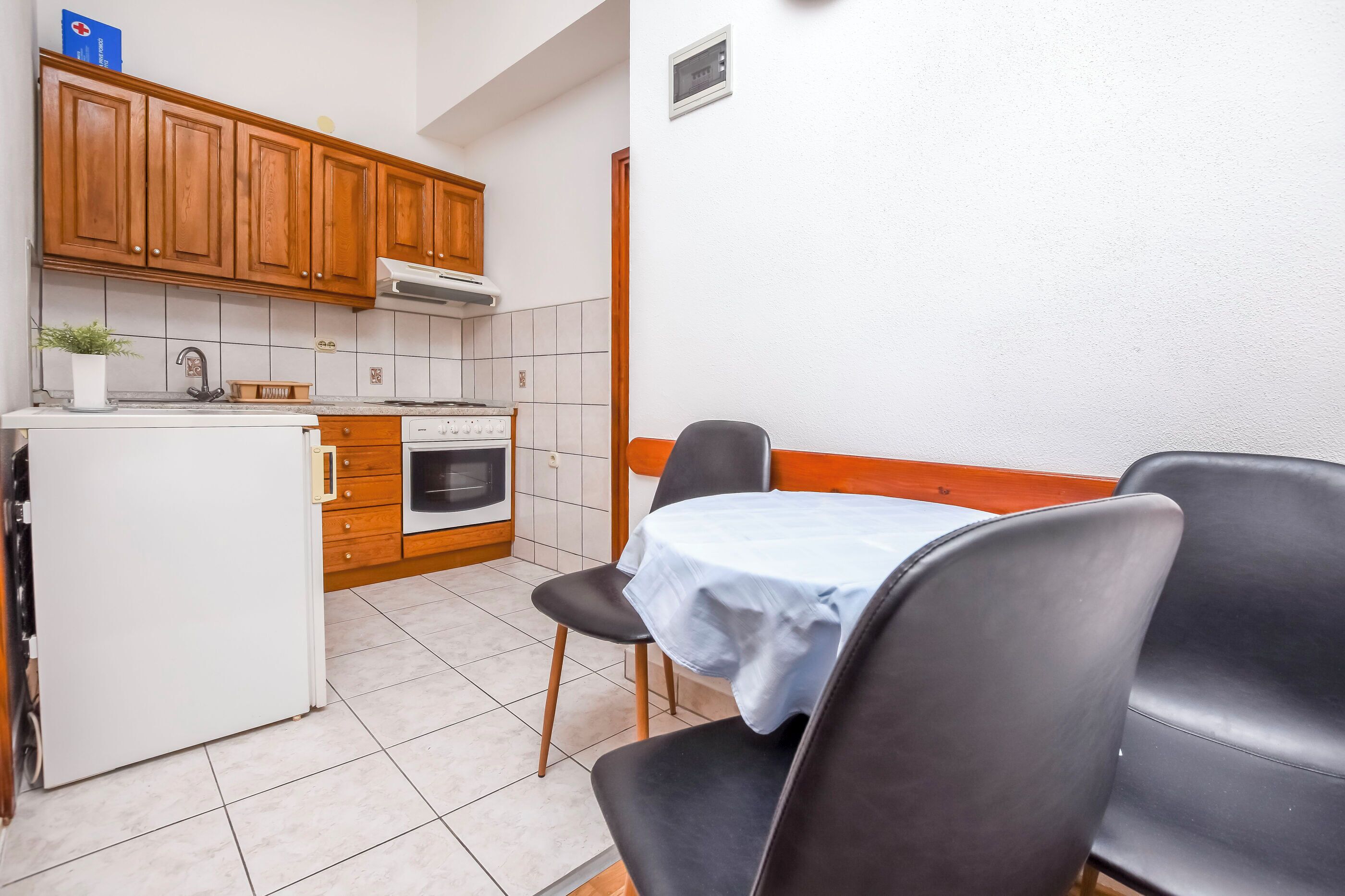 A compact kitchen with wooden cabinets, a white refrigerator, and a dining area with a table and chairs.
