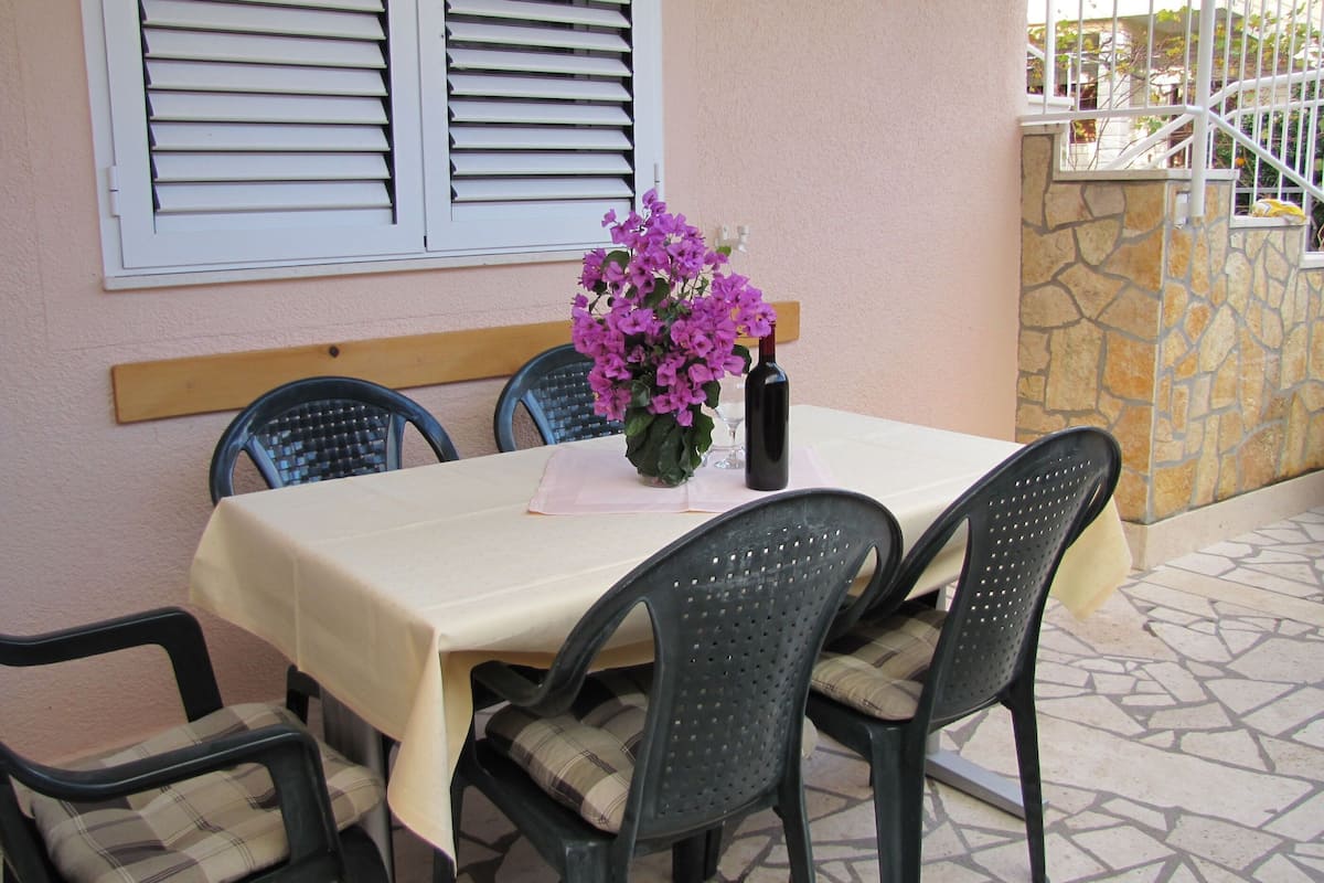 An outdoor dining area with a table set for four, surrounded by chairs with cushioned seats.