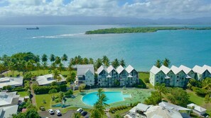 Surrounded by lush greenery and palm trees, this resort features a swimming pool and modern buildings with white roofs.