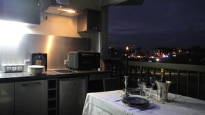 A balcony with a table set for dining, a microwave, and a small kitchen area with cabinets and a sink.