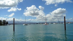 A marina with multiple sailboats docked, calm water, and a clear sky with clouds.