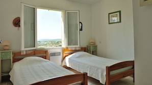 A bedroom with two wooden beds, a window with a view, and a small bedside table with a lamp. - Independent villa at the foot of Mt Ventoux (BEDOIN)