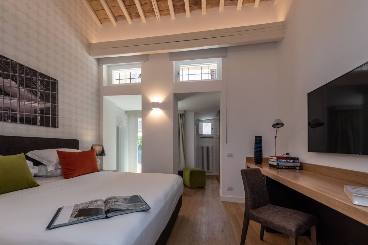 A modern hotel room with a large bed, a desk, a chair, and a TV.