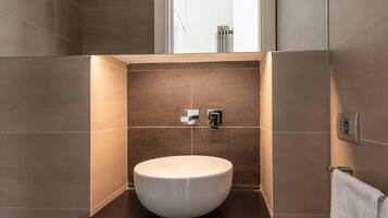 A modern bathroom with a large sink, wooden drawers, and a window above the mirror.