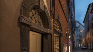 A narrow cobblestone street with historic buildings, a stone archway, and a lit signboard. - Laurina 33 (Rome)