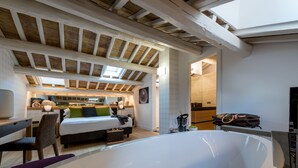 A spacious bedroom with a large white bathtub, a bed with a green and white headboard, and a wooden ceiling with skylights. - Laurina 33 (Rome)