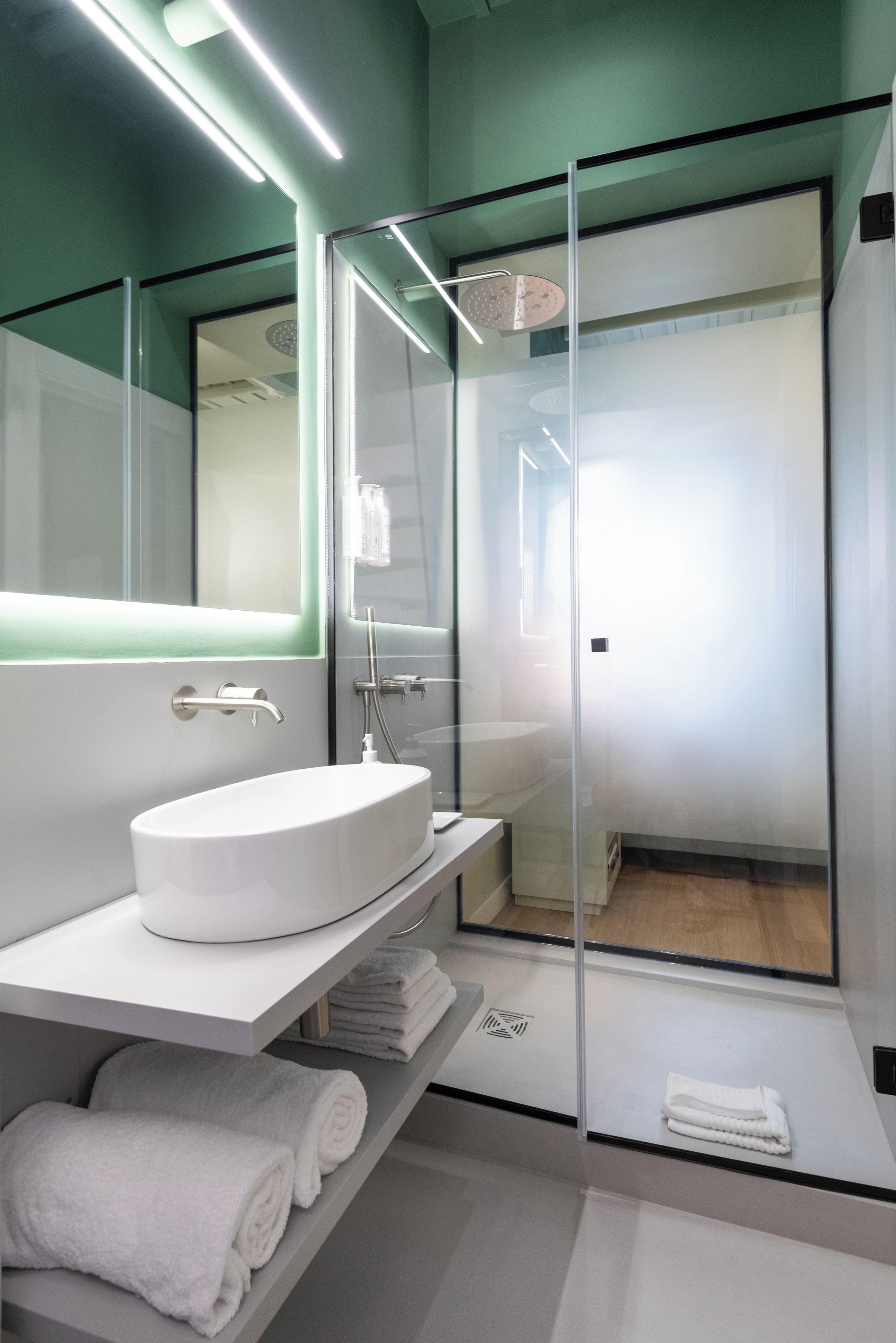 Een moderne badkamer met een douchecabine van glas, een witte wastafel en een spiegel erboven.
