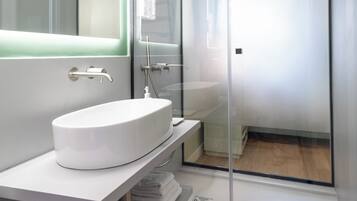 Een moderne badkamer met een douchecabine van glas, een witte wastafel en een spiegel erboven.