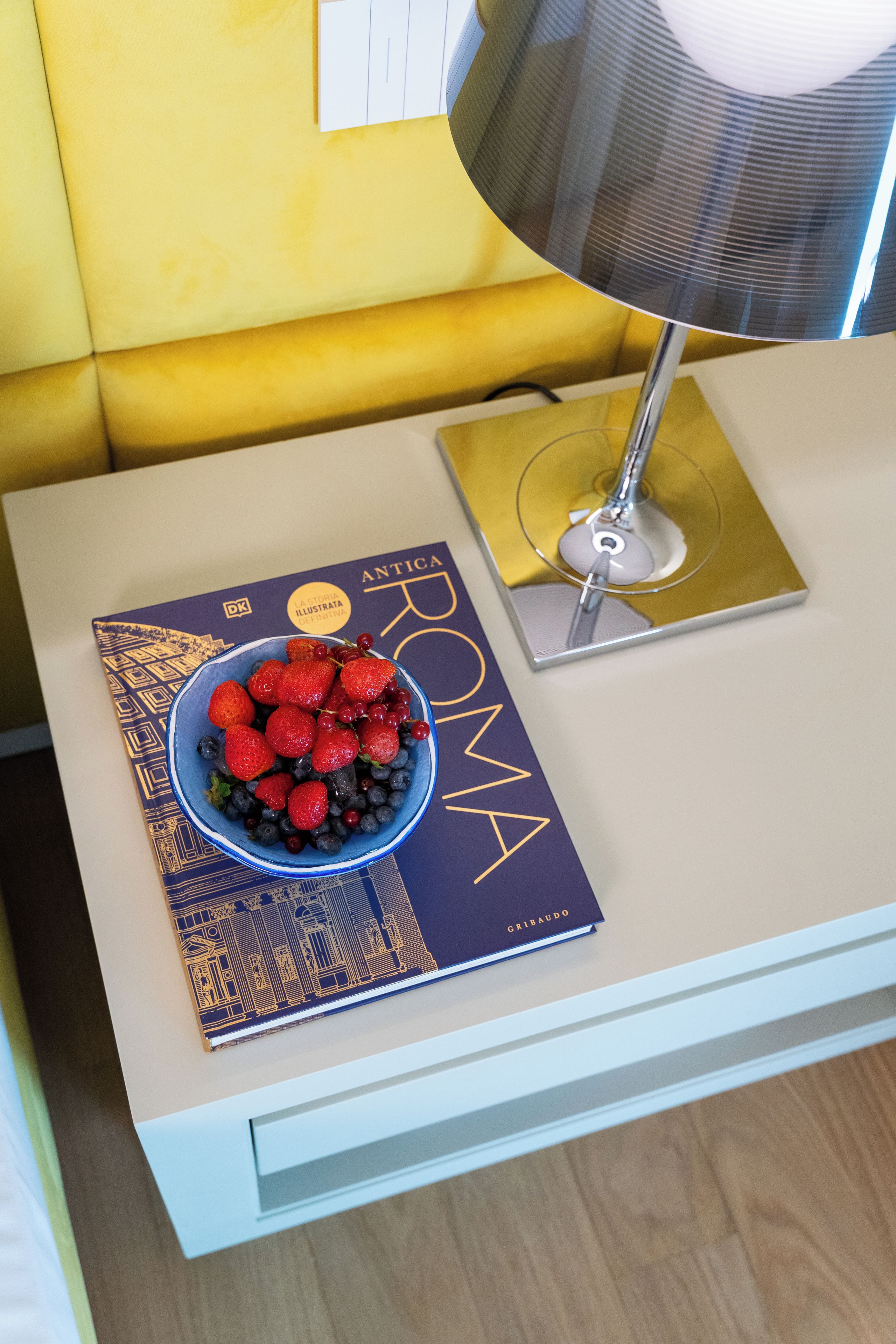 Un libro titulado 'ANTICA' sobre una mesa con un frutero.