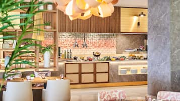 Un restaurant moderne avec des meubles en bois, un îlot central où sont présentés divers plats, et un luminaire décoratif suspendu au plafond.