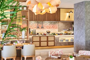 A modern restaurant with wooden furniture, a central island with a variety of dishes, and a decorative hanging light fixture. - Zafiro Palace Andratx (Andraitx)