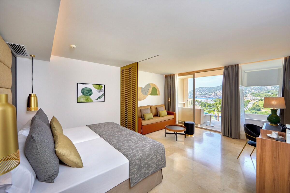Ett modernt hotellrum med en stor säng, en soffa, ett litet bord och utsikt över staden.