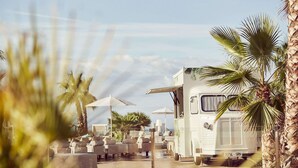 Un camping-car blanc est garé à côté d’un espace piscine équipé de chaises longues et de parasols.