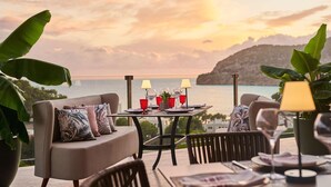 Una terraza con una mesa lista para dos personas, un sofá y vista al mar al atardecer.